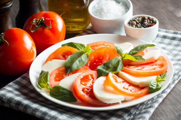 Photo of Caprese Salad with tomatoes, basil, mozzarella, olives and olive oil on wooden background....