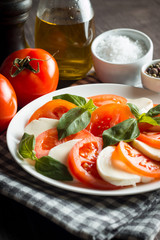 Photo of Caprese Salad with tomatoes, basil, mozzarella, olives and olive oil on wooden background. Italian traditional caprese salad ingredients. Mediterranean, organic and natural food concept.