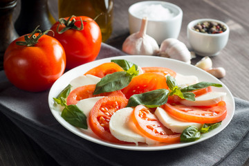 Photo of Caprese Salad with tomatoes, basil, mozzarella, olives and olive oil on wooden background. Italian traditional caprese salad ingredients. Mediterranean, organic and natural food concept.