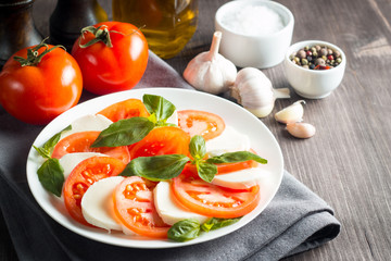 Photo of Caprese Salad with tomatoes, basil, mozzarella, olives and olive oil on wooden background. Italian traditional caprese salad ingredients. Mediterranean, organic and natural food concept.