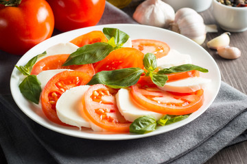 Photo of Caprese Salad with tomatoes, basil, mozzarella, olives and olive oil on wooden background. Italian traditional caprese salad ingredients. Mediterranean, organic and natural food concept.