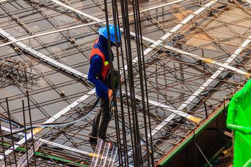 Unidentified worker used the high pressure machine to clean floor slab reinforcement bar with post tension cable tendon on steel form work at the construction site before concreting.