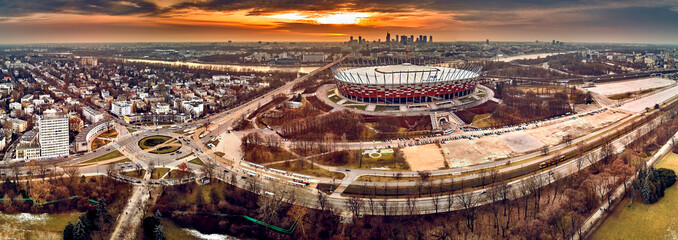 Beautiful panoramic aerial drone view to panorama of Warsaw modern City with skyscraper and The PGE Narodowy National Stadium (Polish: Stadion Narodowy) against the background of a dramatic sunset - obrazy, fototapety, plakaty