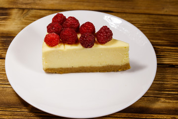 Piece of tasty New York cheesecake with raspberries in a white plate on wooden table