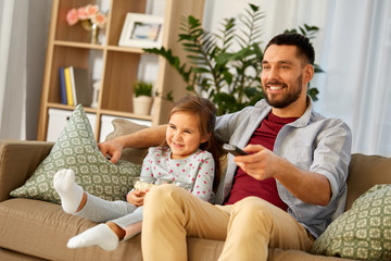 family, fatherhood and people concept - happy father and daughter with popcorn watching tv at home