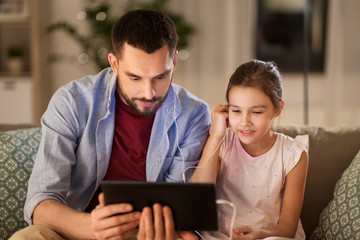 family, fatherhood and technology concept - happy father and little daughter with tablet pc computer and earphones listening to music at home