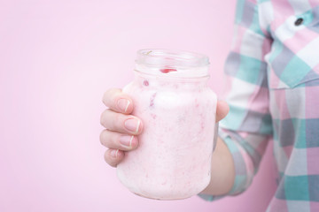 Female hand holds a milk shake closeup with berries on a pink background