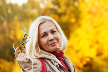 Beautiful Russian middle-aged woman with blue eyes and glasses in the autumn park.