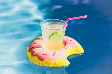 Tasty cocktail with ice and fresh limon on inflatable donut toy at swimming pool.Vacation and relaxation time in the swim pool at summer day. Ripple Water in swimming pool with sunny reflection