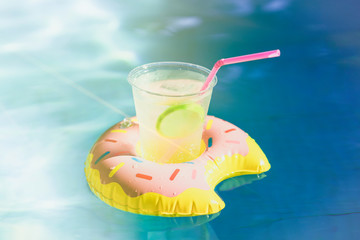 Tasty cocktail with ice and fresh limon on inflatable donut toy at swimming pool.Vacation and relaxation time in the swim pool at summer day. Sunlight effect and Ripple Water reflection