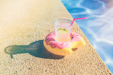 Fototapeta na wymiar Tasty refreshing cocktail on on inflatable donut plastic toy on edge of swimming pool. Ripple Water in swimming pool with sunlight reflection