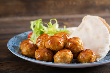 Meatballs in sweet and sour glaze on a plate with pita bread and vegetables in a Moroccan style on a wooden table. Tapas. Trend food.
