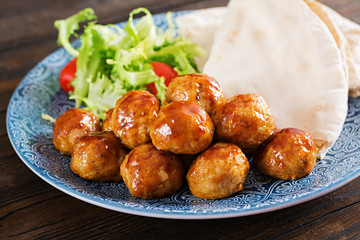 Meatballs in sweet and sour glaze on a plate with pita bread and vegetables in a Moroccan style on a wooden table. Tapas. Trend food.