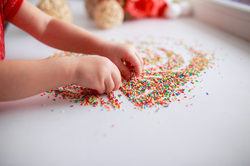 Baby hands in sugar topping. Baby drawing. Baby fingers with candies. Easter sugar topping.