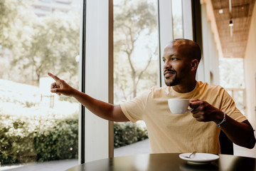 New happy summer day. Young confident African man enjoying his morning coffee and french croissant...