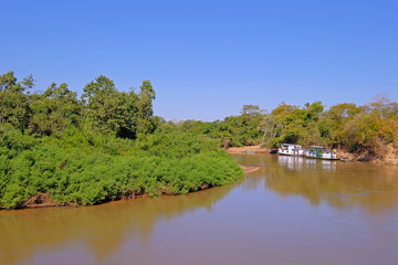Densely forested shores of the Aquidauana river in the brazilian Pantanal, houseboats on the riverbank, Brazil