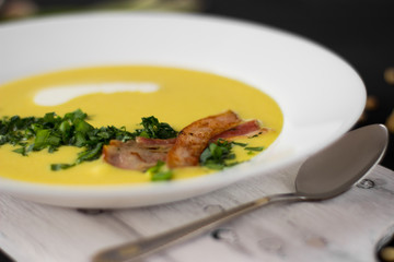 Pea soup with pieces of bacon, parsley and onion in a bowl on a dark background. Pea cream soup. Macro