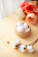 White eggs and eggs in foil on the wooden background with flowers and cotton around. Eggs in the basket