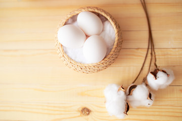 White eggs and eggs in foil on the wooden background with flowers and cotton around. Eggs in the basket
