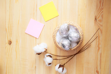 White eggs and eggs in foil on the wooden background with flowers and cotton around. Eggs in the basket