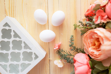 White eggs and eggs in foil on the wooden background with flowers and cotton around. Eggs in the basket