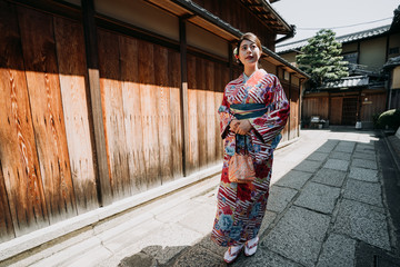 Fototapeta na wymiar full length of young japanese woman in traditional cloth going to visit family in old town in new year walking along the wooden wall on stone road in ishibe alley. local girl in kimono enjoy sunlight