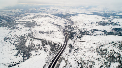 Aerial view of winter asphalt highway or motorway road in countryside with cars and cargo logistic trucks in winter time