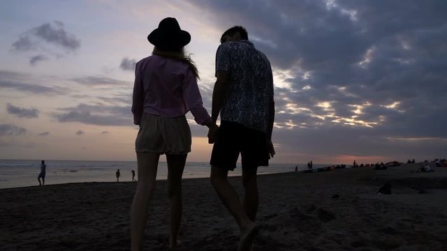 Young couple in love walking, holding hands during sunset on beach, slow motion