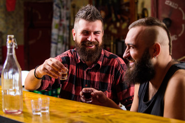 Hipster brutal man drinking alcohol with friend at bar counter. Men drunk relaxing at pub having fun. Strong alcohol drinks. Friends relaxing in pub. Men drinking alcohol together. Alcohol addiction