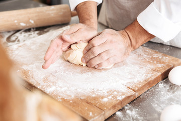 Сropped portrait of male hands mixing dough for pastry, on table at bakery or kitchen