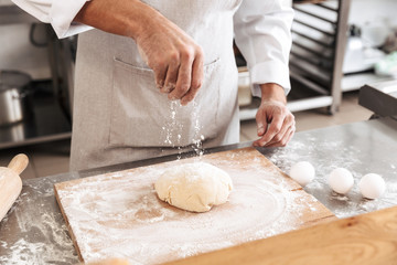 Closeup photo of man chief making dough for bread, on table at bakery or kitchen