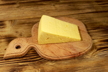 Piece of cheese on cutting board on wooden table