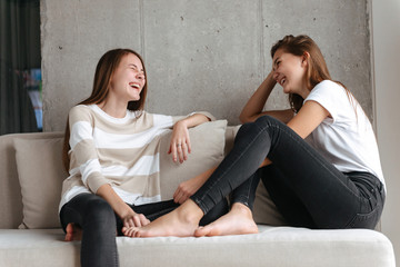 Two cheerful girls talking while sitting at home