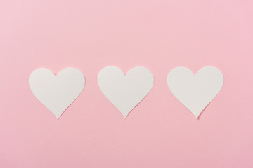 white paper hearts arranged in row on pink background