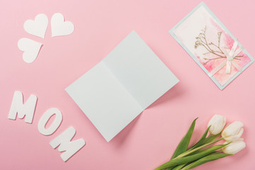 blank and decorated mothers day greeting cards, white tulips, papers hearts and word mom on pink background