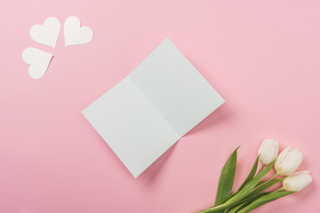 white blank greeting card, paper hearts and white tulips on pink background