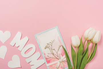 mothers day postcard decorated with dried plant and bow, white tulips, paper hearts and word mom on pink background