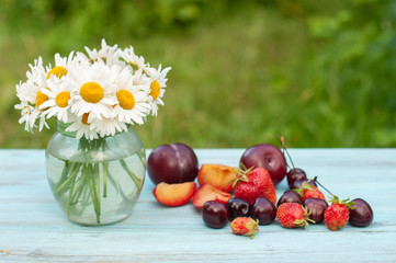 Berries, fruits and a bouquet of daisies on a wooden table in the garden. Summer concept