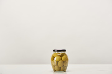 glass can of conserved olives on white surface