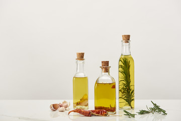 bottles of oil flavored with rosemary and various spices on white surface