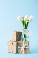 gift boxes, greeting card and bouquet of white tulips with happy mothers day greeting label on blue background