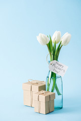 gift boxes and bouquet of white tulips with happy mothers day greeting label on blue background