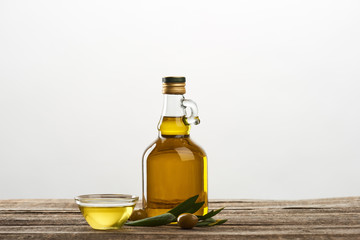 bottle and bowl with oil, olives and olive tree leaves isolated on grey