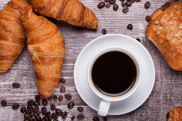 Cup of hot coffee and freshly baked croissants on dark wooden table