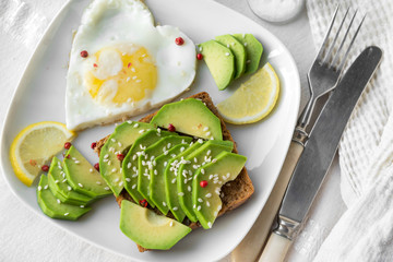 sandwich with avocado, sesame seeds, scrambled eggs, a slice of lemon on the plate, fork, knife