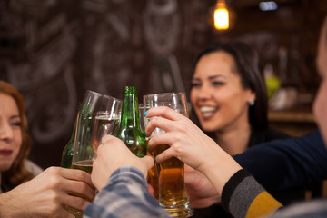 Happy young friends clinking beer bottles in vintage old styled pub