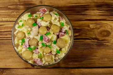 Potato salad with marinated mushrooms, sausage, onion and mayonnaise on wooden table