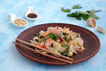 Refreshing salad with pomelo, shrimps, carrots and cashew nuts on a light blue background. Asian cuisine.