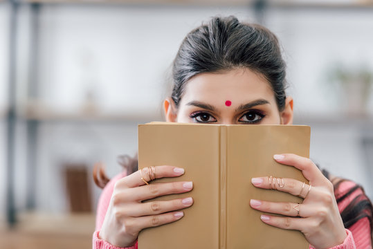 indian student with bindi holding book in front of the face