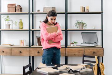 sad indian student with bindi looking at notebooks at home